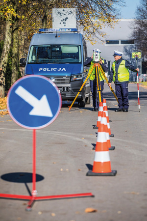 na zdjęciu dwóch policjantów w kamizelkach odblaskowych stoi przy radiowozie marki volkswagen crafter 2,0 TDI, przed nimi czerwono-białe słupki i niebieski znak z białą strzałką skierowaną w dół