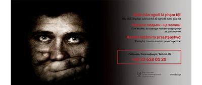 &quot;Billboard dotyczący handlu ludźmi. Tło stanowi zdjęcie mężczyzny, któremu ktoś zasłania usta. Na grafice w kilku językach tekst: Handel ludźmi to przestępstwo! Pamiętaj, zawsze możesz prosić o pomoc. Zadzwoń +48 22 628 01 20&quot;