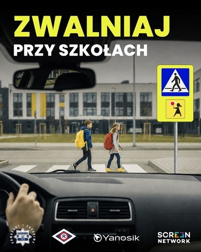 "Plakat z napisem zwalniaj przy szkołach. W tle dwoje dzieci na przejściu dla pieszych widziane przez szybę samochodu zbliżającego się do tego przejścia. Dzieci mają na plecach tornistry."