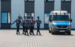 &quot;Sześciu policjantów kompanii honorowej idzie ze złożoną flagą  i sztandarem, obok radiowóz&quot;