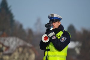 &quot;Policjant ruchu drogowego widoczny od pasa w górę, podczas wykonywania pomiaru prędkości ręcznym miernikiem.&quot;