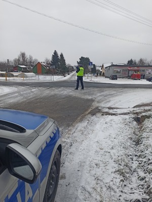 Policjant ruchu drogowego mierzy prędkość.  Na zdjęciu widoczny radiowóz oraz zaśnieżona droga