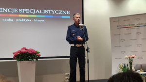 &quot;policjant przed mikrofonem stoi na tle ekranu wyświetlającego tytuł konferencje specjalistyczne&quot;