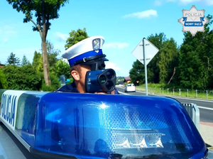 &quot;policjant z laserowym miernikiem prędkości, obok niebieska lampa na dachu radiowozu z napisem POLICJA - poziom&quot;&gt;