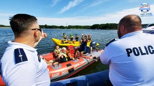 &quot;dwaj policjanci na policyjnej łodzi - widok z tyłu, przed nimi widoczni są dorośli i dzieci na motorówce i na tzw. bananie&quot;