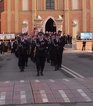 Przemarsz sztandarów i uczestników uroczystości Święta Niepodległości na Rynek. W przemarszu również sztandar Komendy Powiatowej Policji w Proszowicach