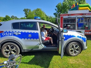 Dzień Dziecka Ostrów. Na zdjęciach widać, w którym siedzą dzieci oraz siedzącą przy stole policjantkę robiącą odciski palców. jedna z dziewczynek rozwiązuje rebus.