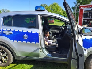 Dzień Dziecka Ostrów. Na zdjęciach widać, w którym siedzą dzieci oraz siedzącą przy stole policjantkę robiącą odciski palców. jedna z dziewczynek rozwiązuje rebus.