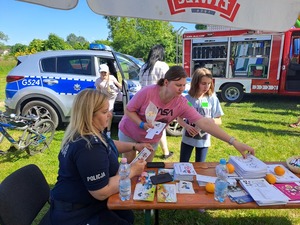 Dzień Dziecka Ostrów. Na zdjęciach widać, w którym siedzą dzieci oraz siedzącą przy stole policjantkę robiącą odciski palców. jedna z dziewczynek rozwiązuje rebus.