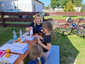 Dzień Dziecka Ostrów. Na zdjęciach widać, w którym siedzą dzieci oraz siedzącą przy stole policjantkę robiącą odciski palców. jedna z dziewczynek rozwiązuje rebus.