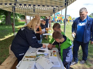 Stoisko Policji, przy którym dorośli i dzieci odbierają upominki i robią odciski palców.