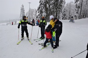 &quot;na szczycie stoku policjanci rozmawiają z chłopcem na temat bezpiecznej jazdy na nartach, jeden z nich wręcza mu element odblaskowy&quot;