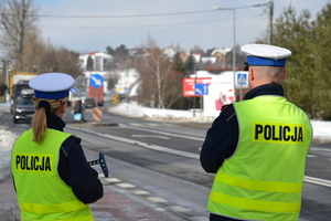 &quot;Policjantka oraz policjant ruchu drogowego stoją nieopodal przejścia dla pieszych i nadzorują ruch&quot;