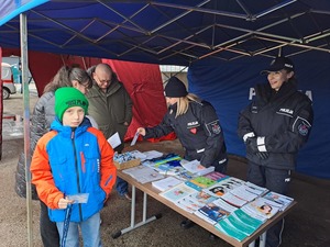 Stoisko edukacyjno-informacyjne wystawione w ramach WOŚP, wraz z materiałami edukacyjnymi, gadżetami. Przy stoisku osoby zainteresowane oraz policjanci z KPP Proszowice.