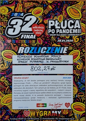 Stoisko edukacyjno-informacyjne wystawione w ramach WOŚP, wraz z materiałami edukacyjnymi, gadżetami. Przy stoisku osoby zainteresowane oraz policjanci z KPP Proszowice.